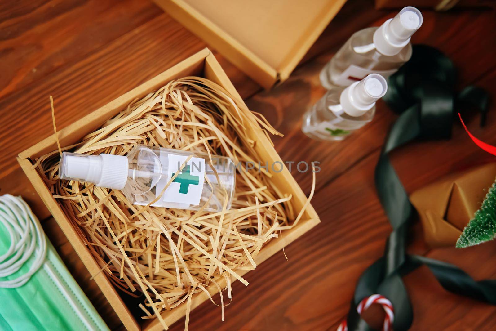 Top view of box of straw and antiseptic. Gift against coronavirus, sanitizers, medical masks and a satin ribbon on wooden table. Concept of fighting virus and bacteria in quarantine.