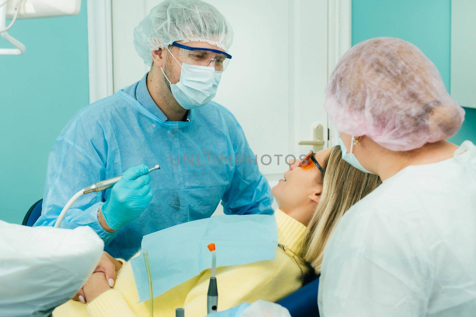 The patient smiles in the dentist's chair in a protective mask and instrument before treatment in the dental office by Lobachad