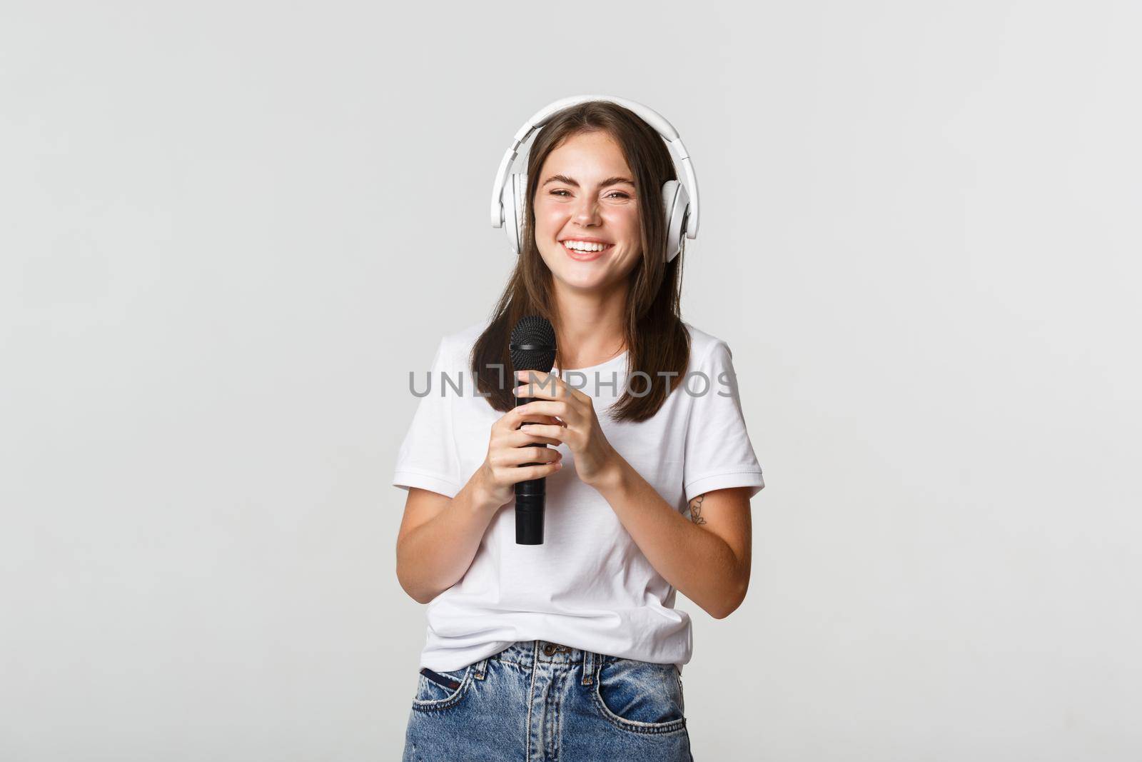 Attractive smiling brunette girl in headphones, singing karaoke, holding microphone.