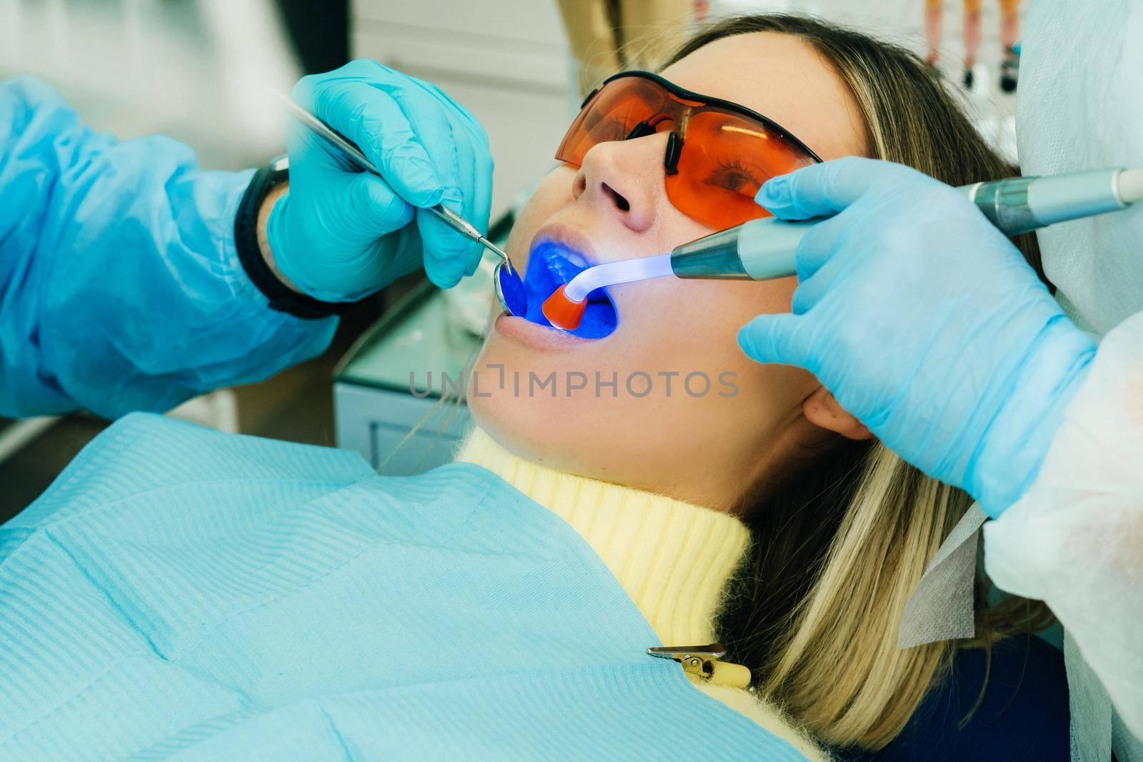 A young beautiful girl in dental glasses treats her teeth at the dentist with ultraviolet light. filling of teeth by Lobachad