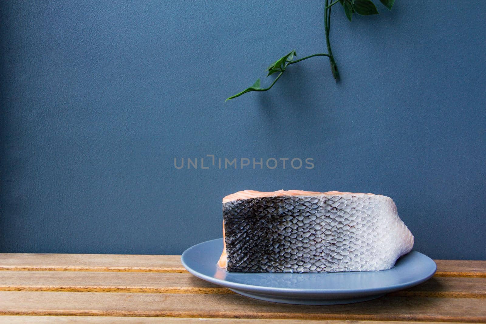 Salmon fresh fish lay on rustic table and blue background and wait to be cooked. Green leaf hand from window.