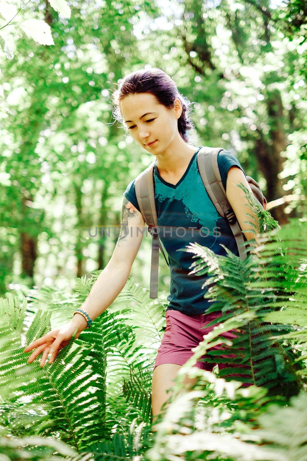Explorer girl with backpack walking among bushes in summer forest.