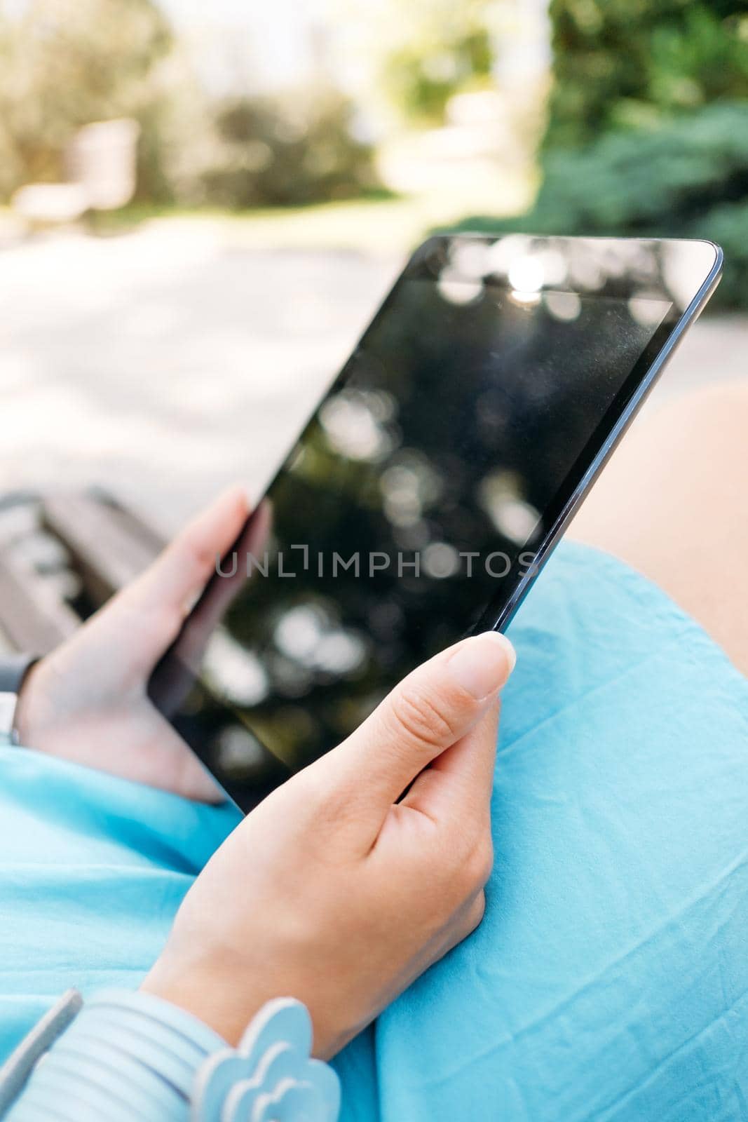 Unrecognizable young woman sitting with digital tablet in the park, close-up of hands.