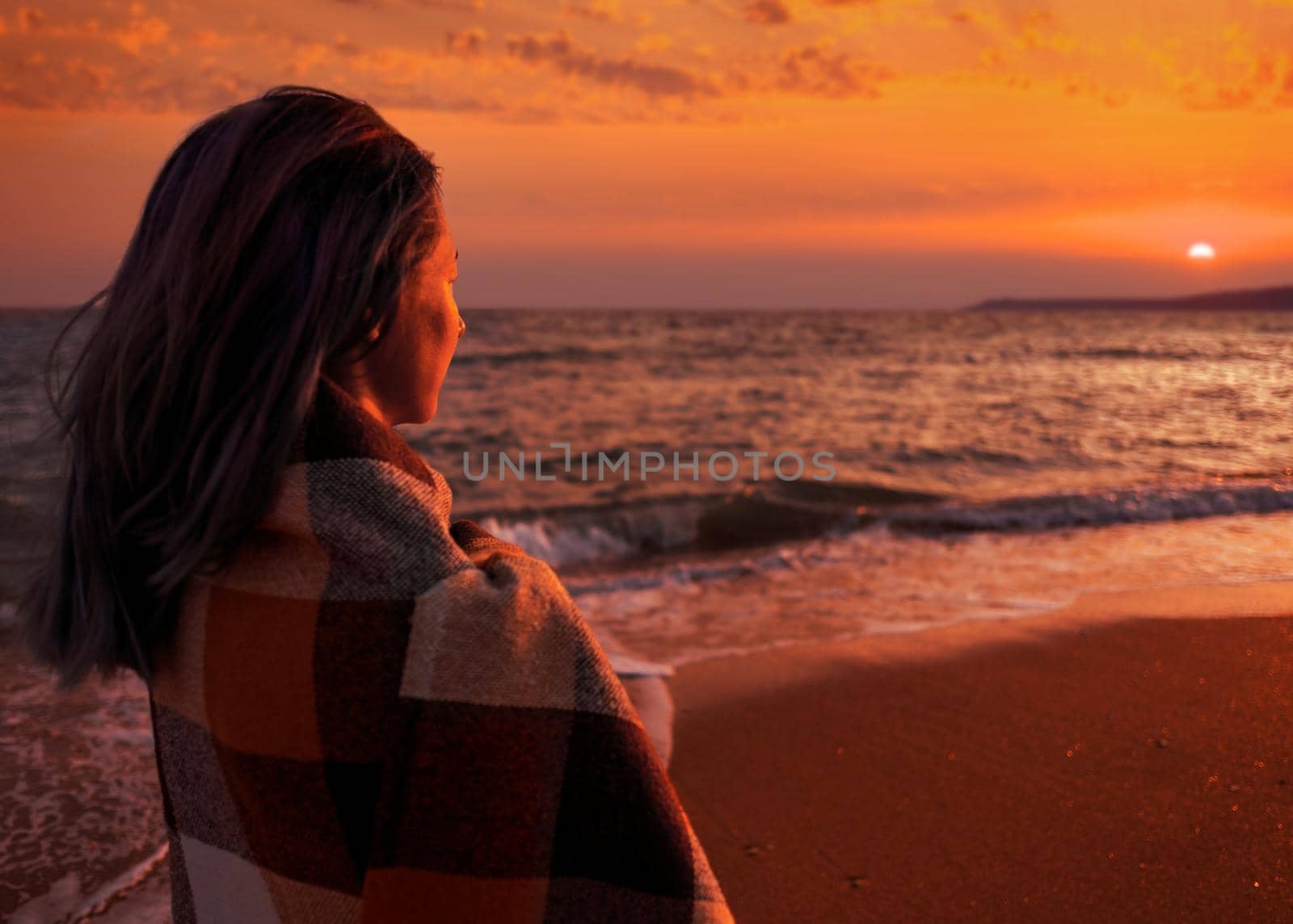 Young woman standing on sand beach and enjoying view of sunset over sea.