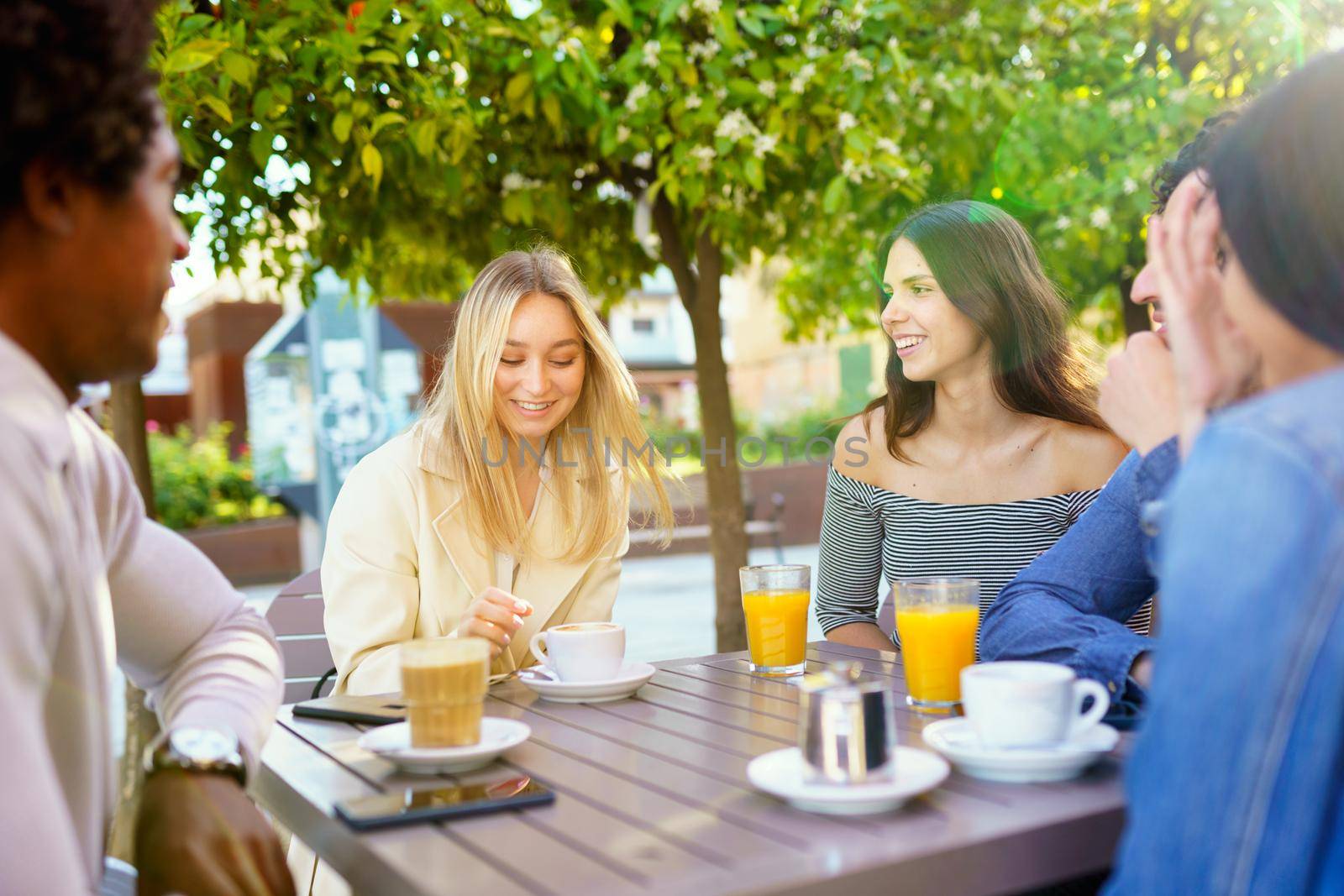 Multi-ethnic group of friends having a drink together in an outdoor bar. Three women and two men in a caf talking, laughing and enjoying their time.