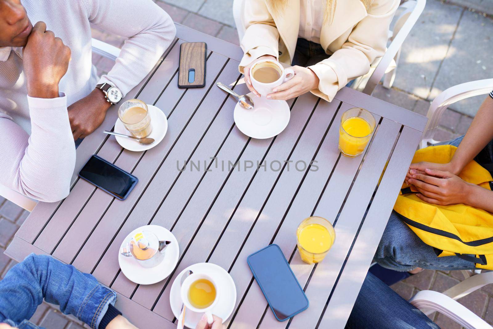 Top view of unrecognizable people drinking some beverages sitting at the table on the terrace of a bar.. Young people having fun together