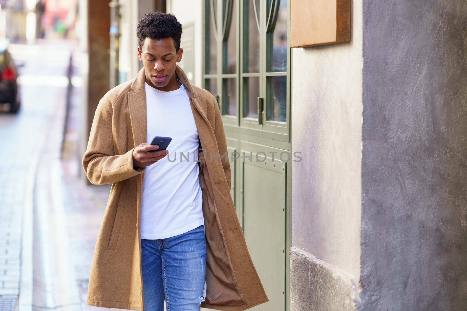 Young black man consulting his phone while walking down the street. Cuban guy in urban background.