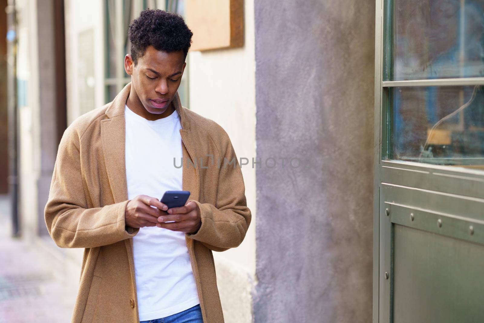 Young black man using his smartphone outdoors. Cuban guy smiling in urban background.