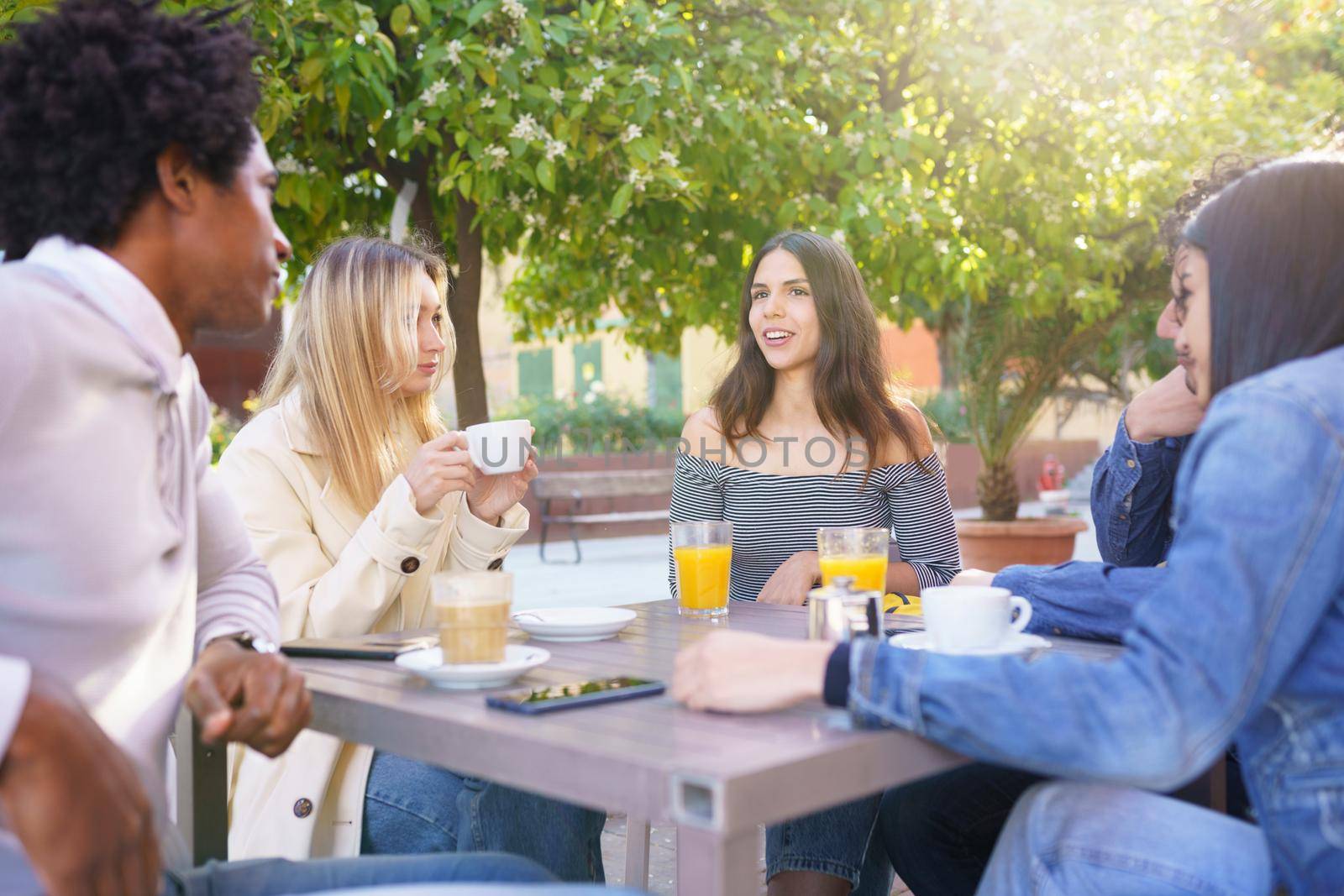 Multi-ethnic group of students having a drink on the terrace of a street bar. by javiindy
