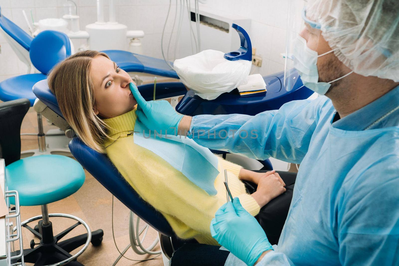 a dentist wearing a protective mask sits down next to the patient and covers his mouth with a finger by Lobachad