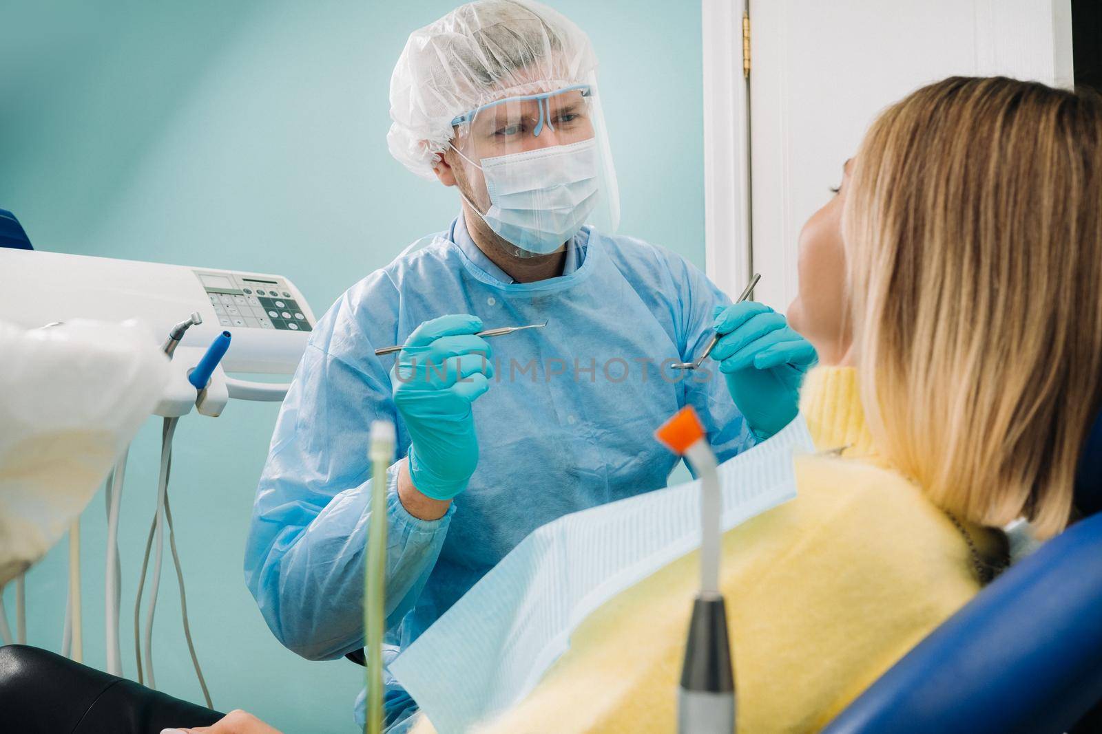 a dentist wearing a protective mask sits nearby and holds instruments in his hands before treating a patient in the dental office.