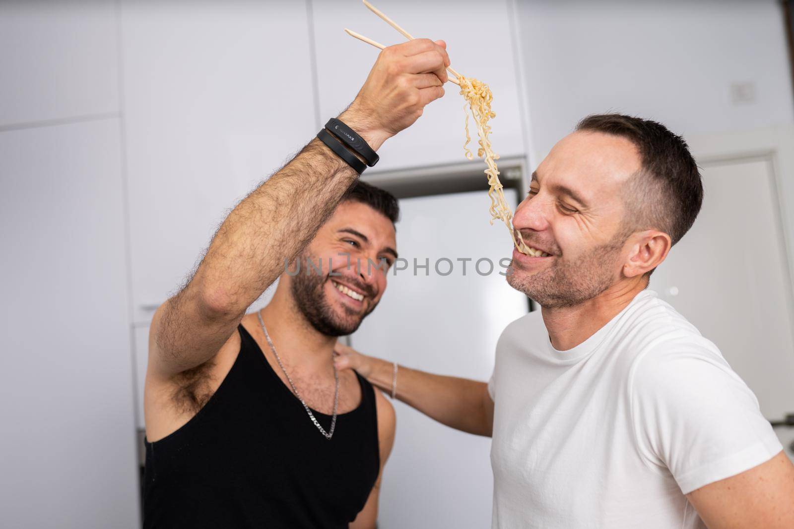 Man feeding pasta to his boyfriend in a fun way. Homosexual relationship concept.