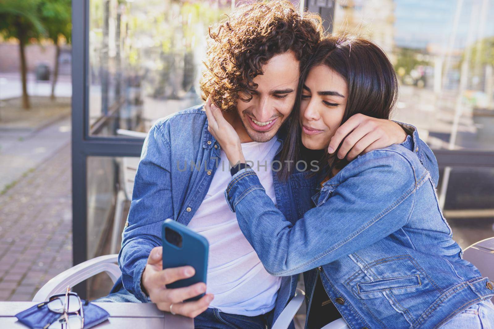 Arab couple looking at pictures taken with their smartphone, sitting on the terrace of a bar.