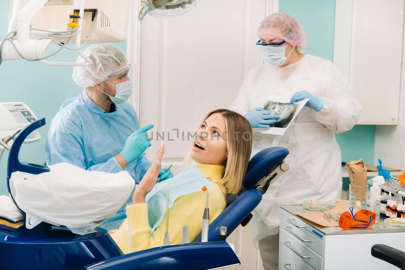 The dentist explains the details of the X-ray to his colleague, the patient is surprised by what is happening.