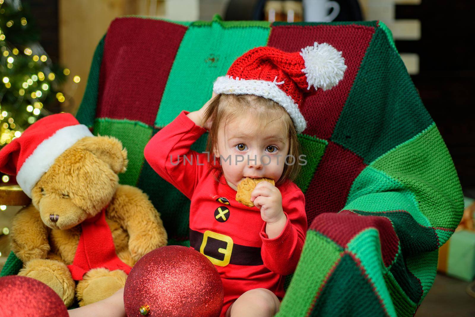 Cute baby face in Santa hat near Christmas tree tasting christmas sweet treats. Happy Childhood, child 1 year old. New year kids