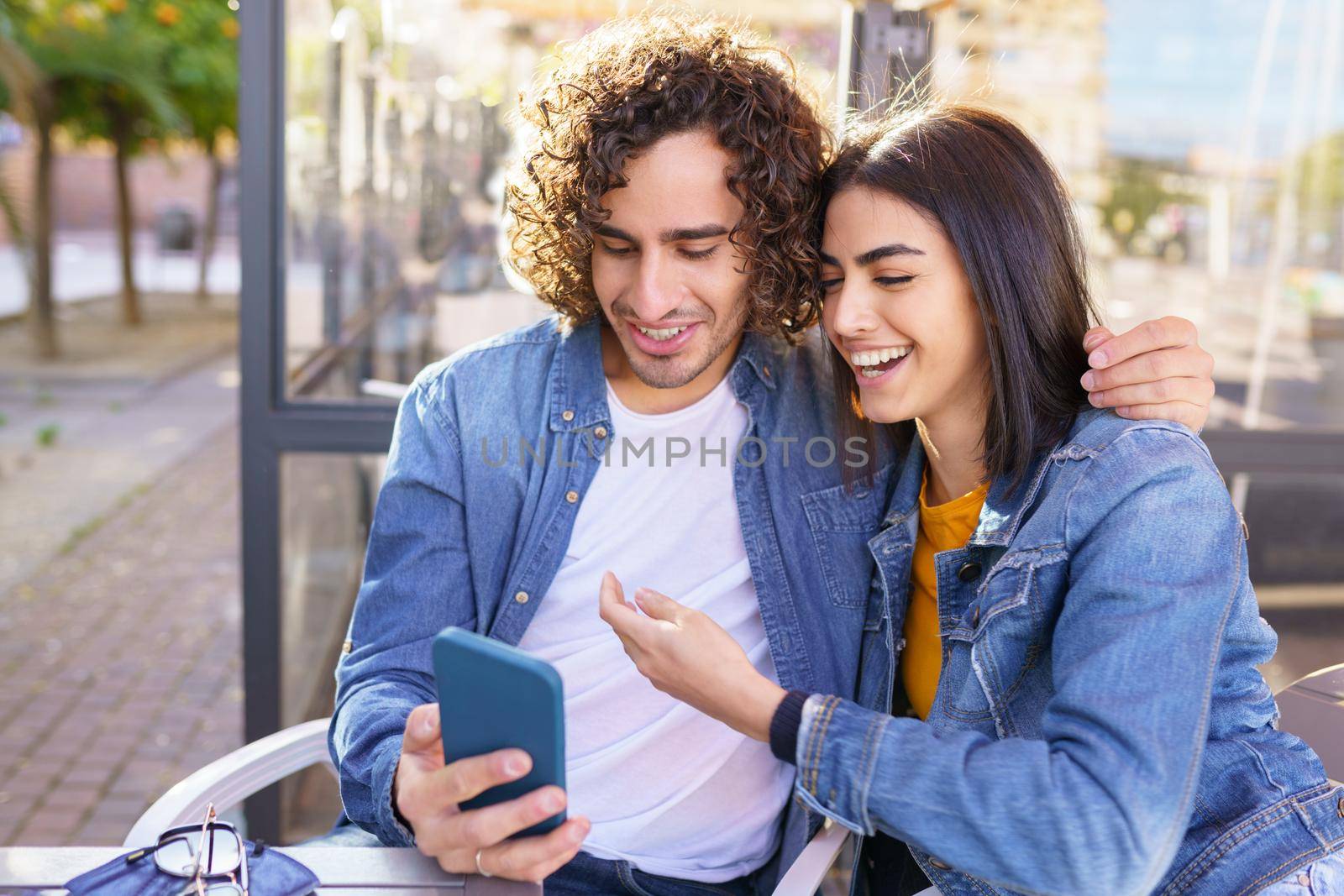 Arab couple looking at pictures taken with their smartphone, sitting on the terrace of a bar.
