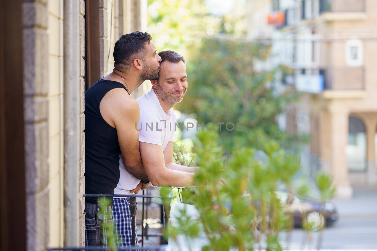 Gay couple in a romantic moment leaning out of their balcony. Homosexual lifestyle concept.