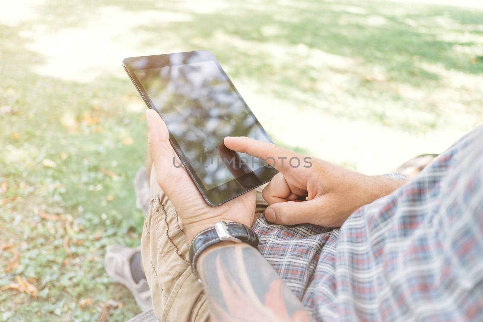 Close-up image of male hands with digital tablet in the park.