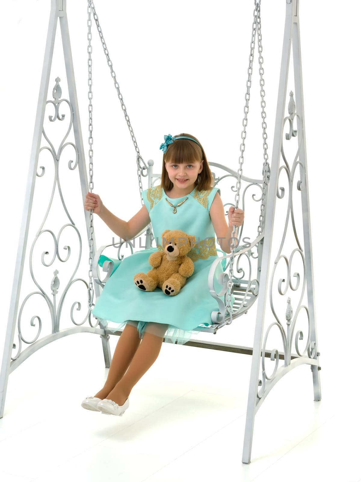 A little girl swings on a swing with a teddy bear. The concept of a happy childhood, the development of a child in the family. Isolated on white background.