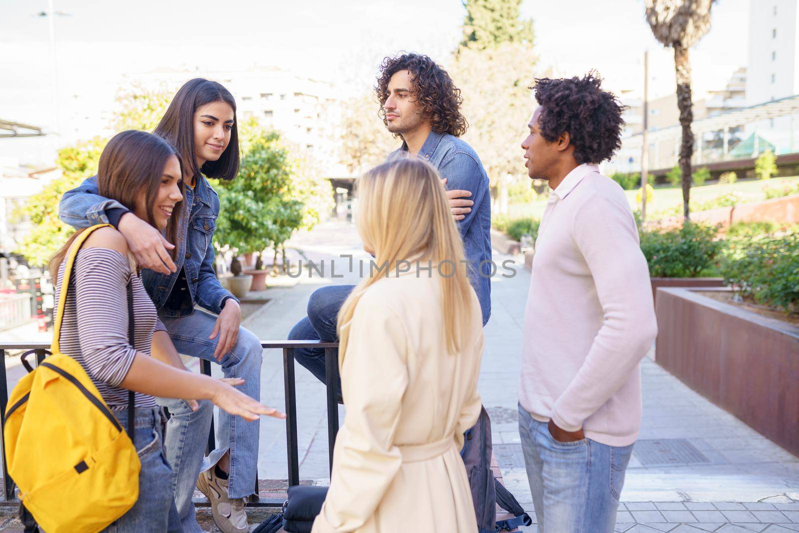 Multi-ethnic group of friends gathered in the street leaning on a railing. Young people having fun together.