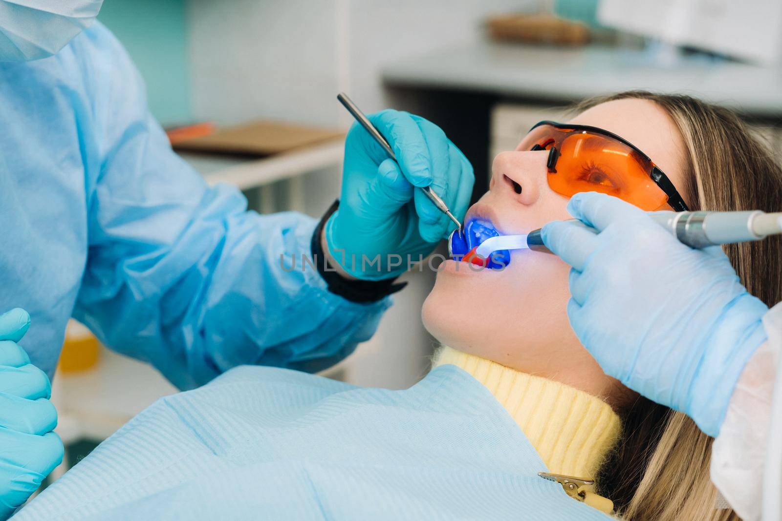 A young beautiful girl in dental glasses treats her teeth at the dentist with ultraviolet light. filling of teeth.