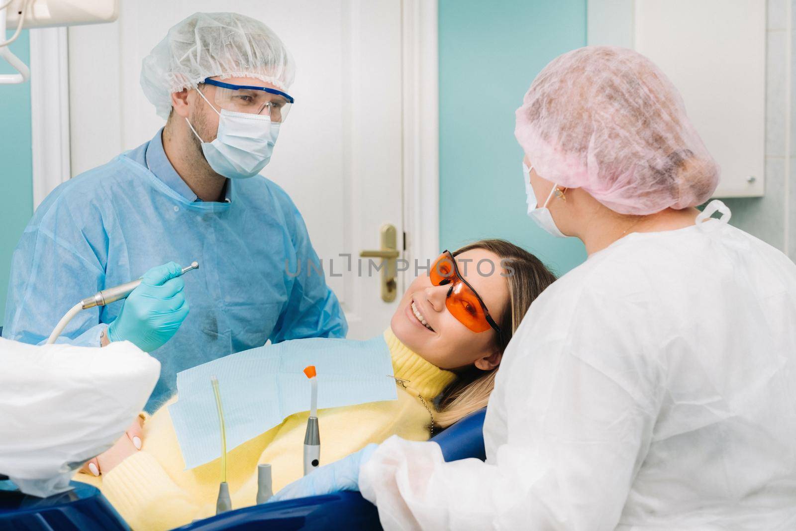 The patient smiles in the dentist's chair in a protective mask and instrument before treatment in the dental office.