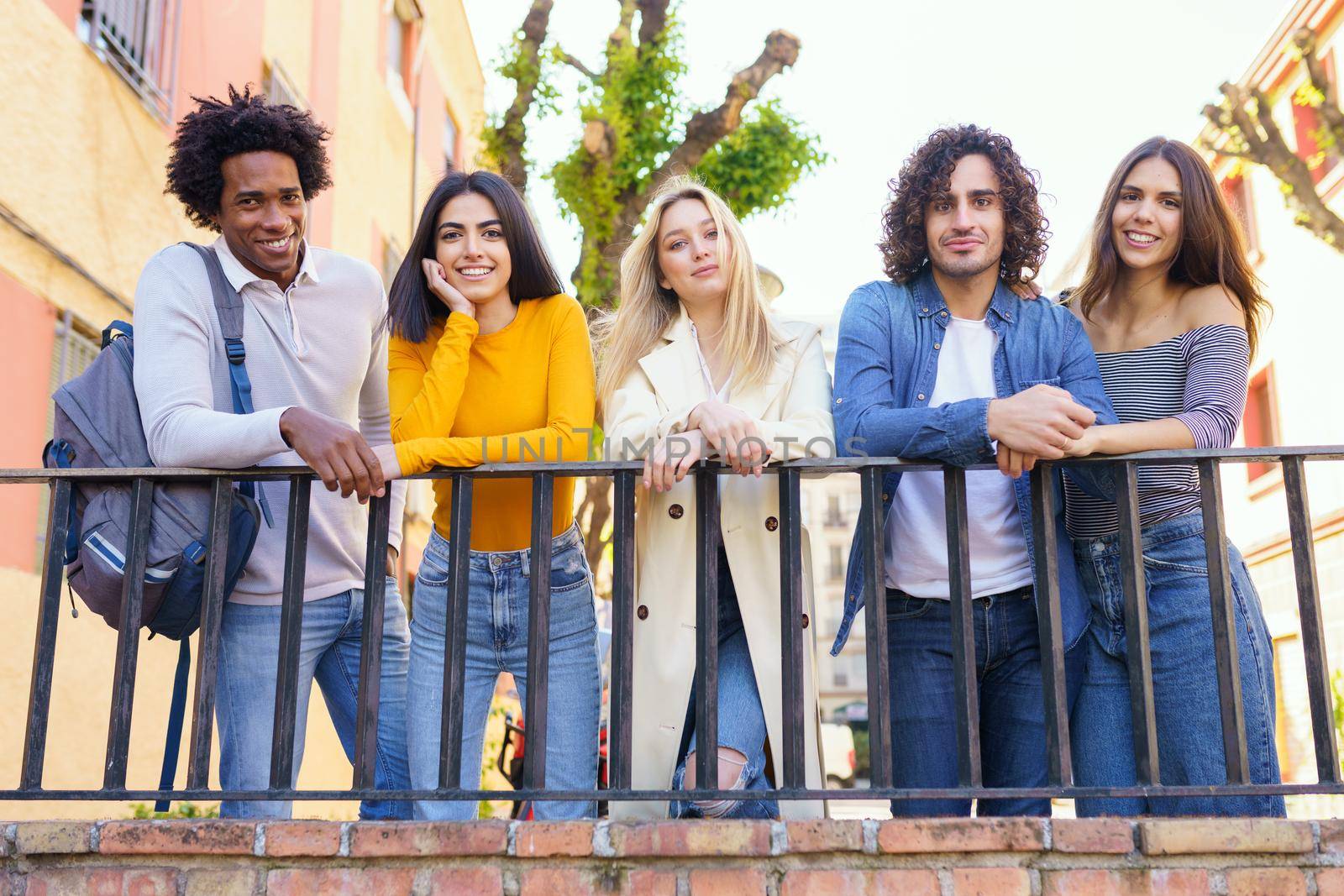 Multi-ethnic group of friends gathered in the street leaning on a railing. Young people having fun together.