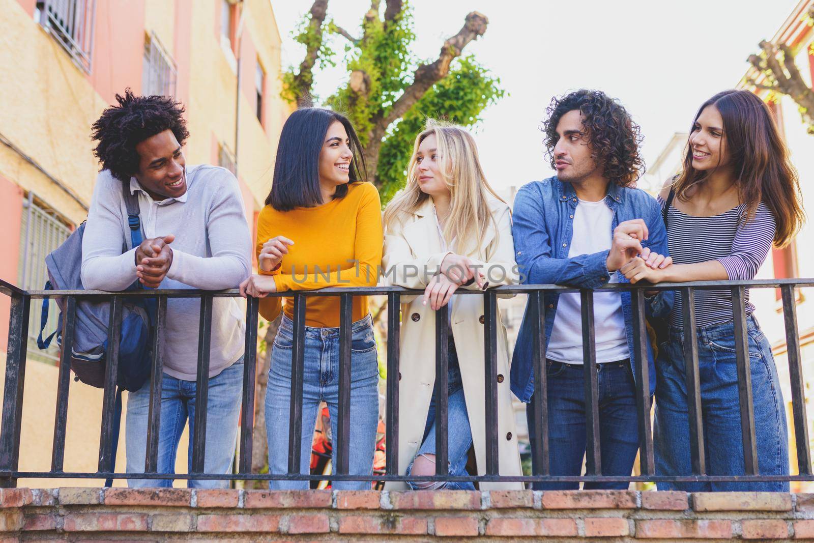 Multi-ethnic group of friends gathered in the street leaning on a railing. Young people having fun together.