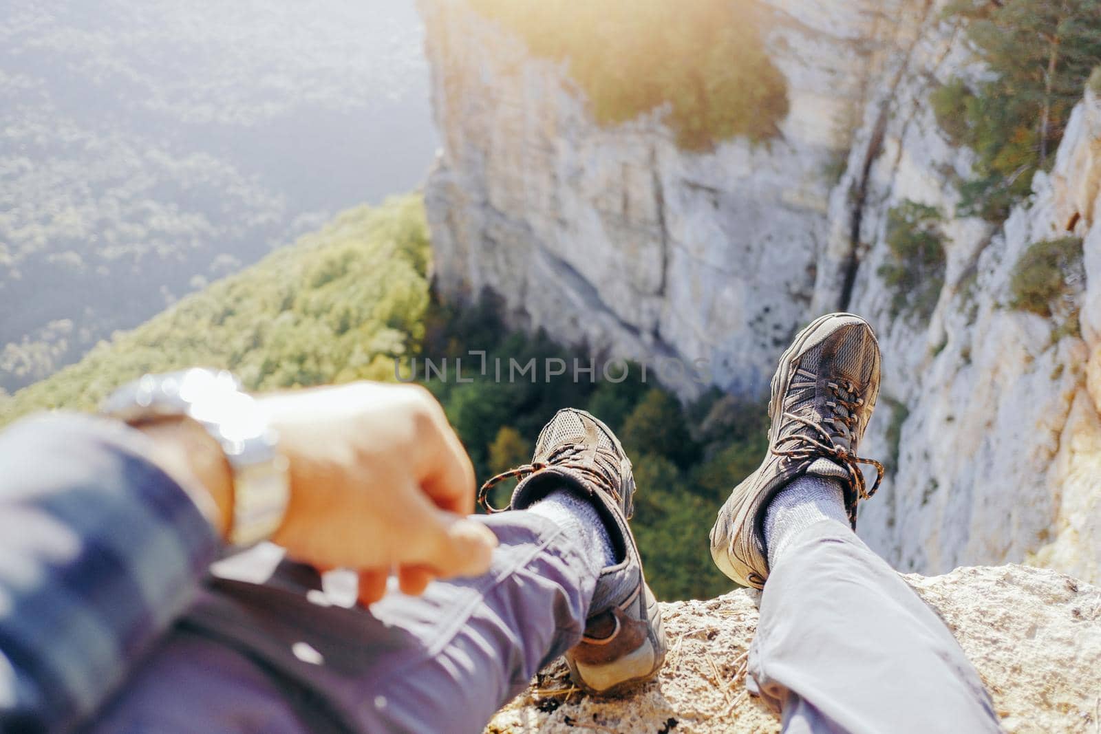 Unrecognizable traveler young man sitting on edge of cliff over valley, view of legs, pov.