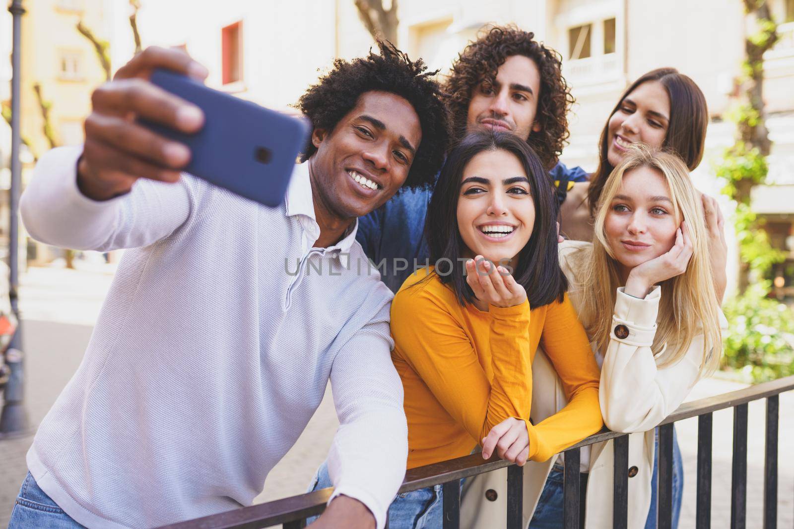Black man with afro hair taking a smartphone selfie with his multi-ethnic group of friends outdoors.