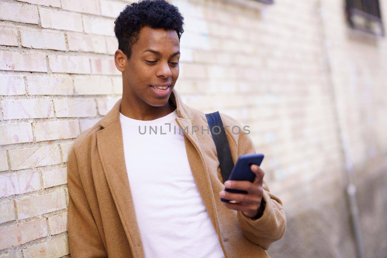 Cuban young man using a smartphone near a urban wall. by javiindy