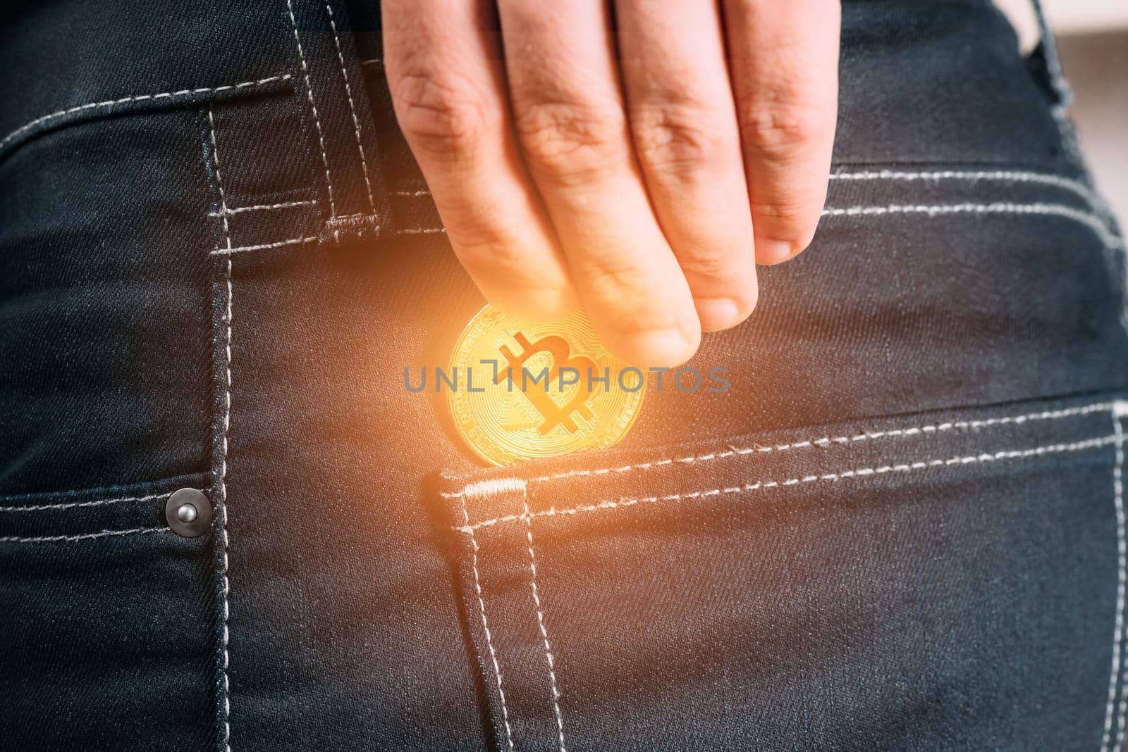 Male hand holding gold bitcoin and putting into pocket of jeans, symbol of crypto currency.