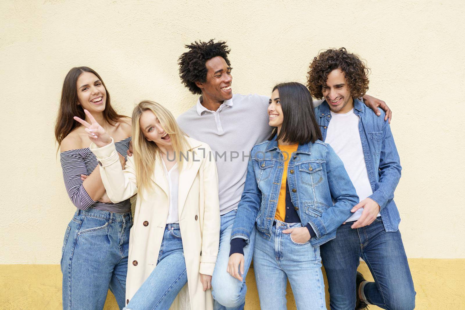 Multi-ethnic group of friends posing while having fun and laughing together against a yellow urban wall.