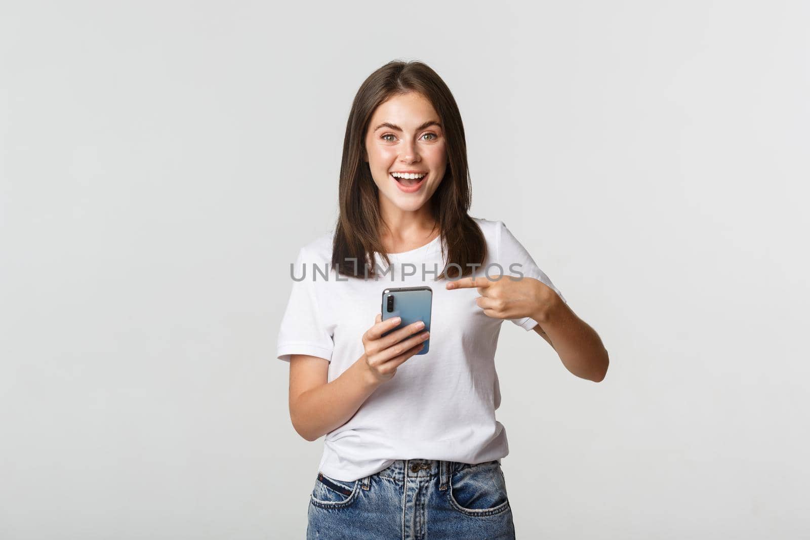 Excited and pleased brunette girl pointing finger at smartphone screen by Benzoix
