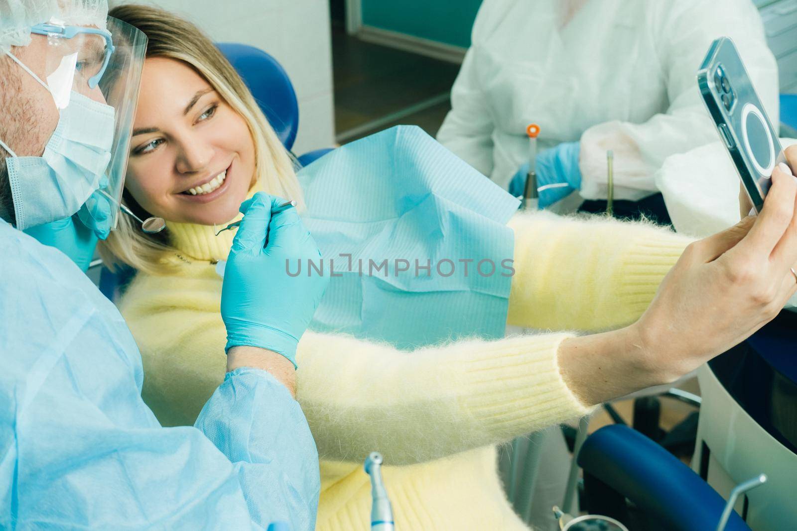 the dentist in a protective mask sits next to the patient and takes a photo after work.