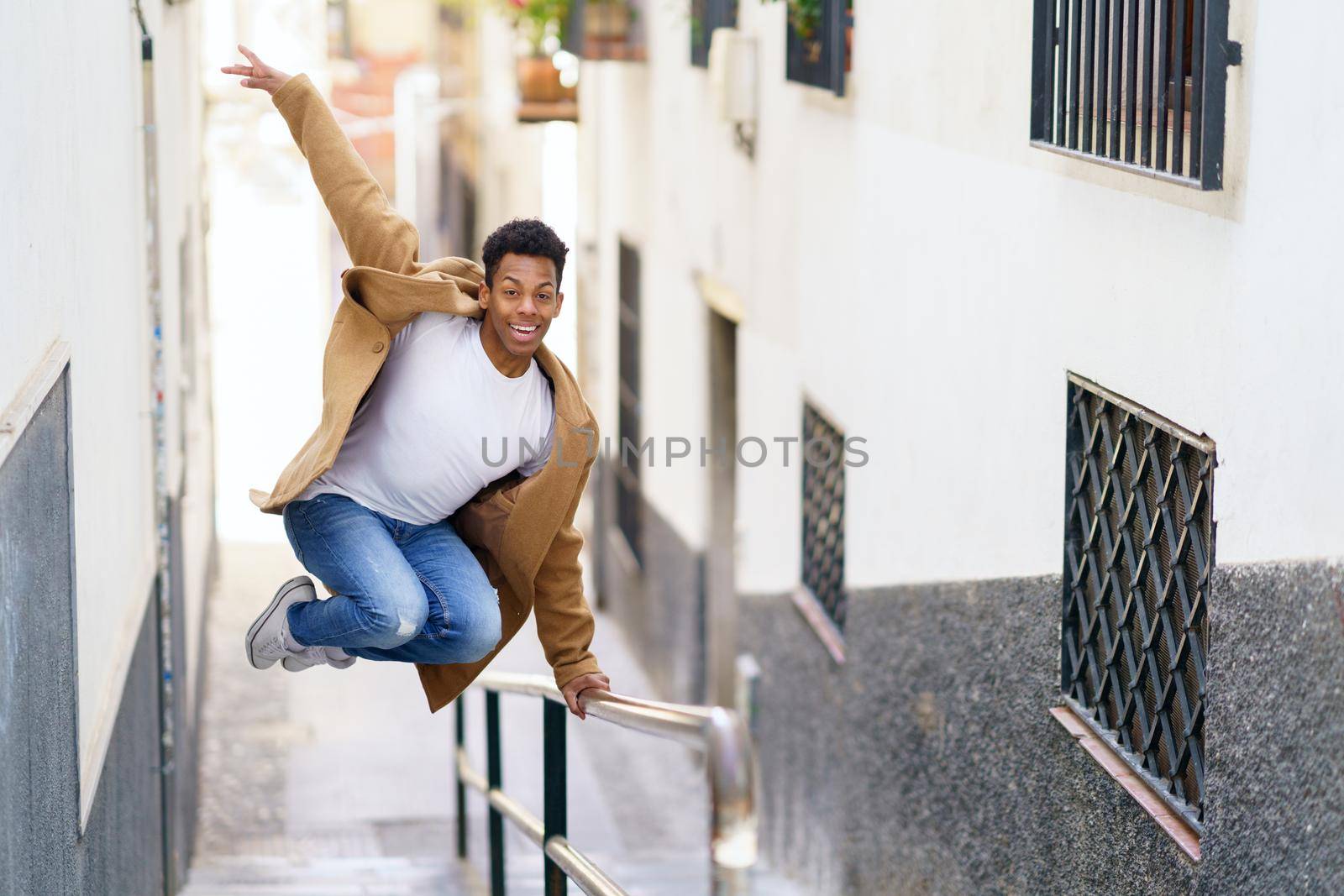 Young black man jumping for joy over a handrail in the street. Cuban guy.