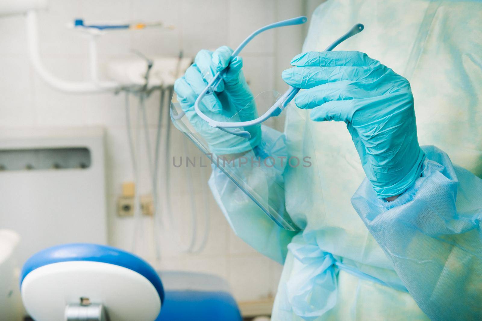 close up of a dentist's hands holding a protective plastic screen in his office by Lobachad