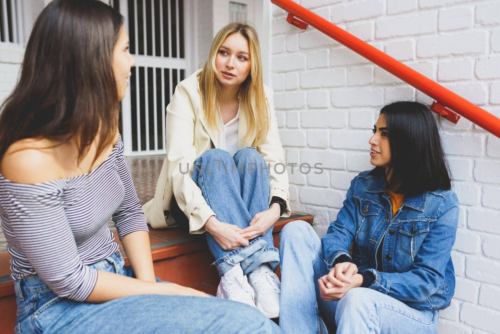 Multi-ethnic group of three female friends sitting on street steps talking.