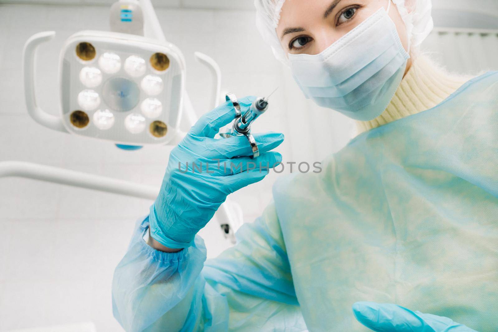 A masked dentist holds an injection syringe for a patient in the office.