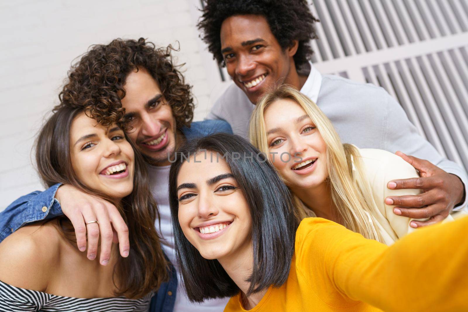 Multi-ethnic group of friends taking a selfie together while having fun in the street. Persian woman in the foreground.