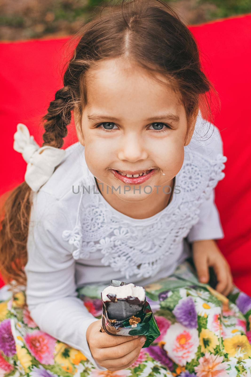 Beautiful little girl eats ice-cream in the summer bright background.