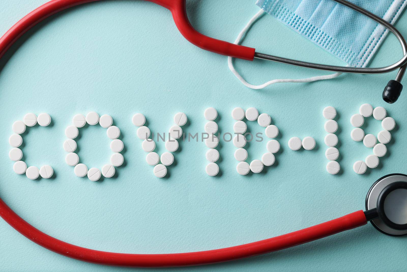 Top view of covid lettering made of tablets, stethoscope tool on surface, protective face mask, prevention coronavirus spread. Illness, antibody, medicine, healthcare, medication concept