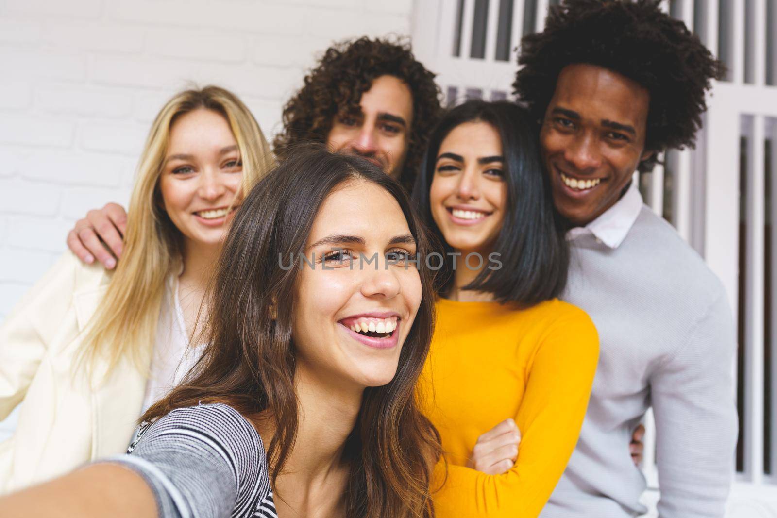 Multi-ethnic group of friends taking a selfie together while having fun in the street. Caucasian girl in the foreground.