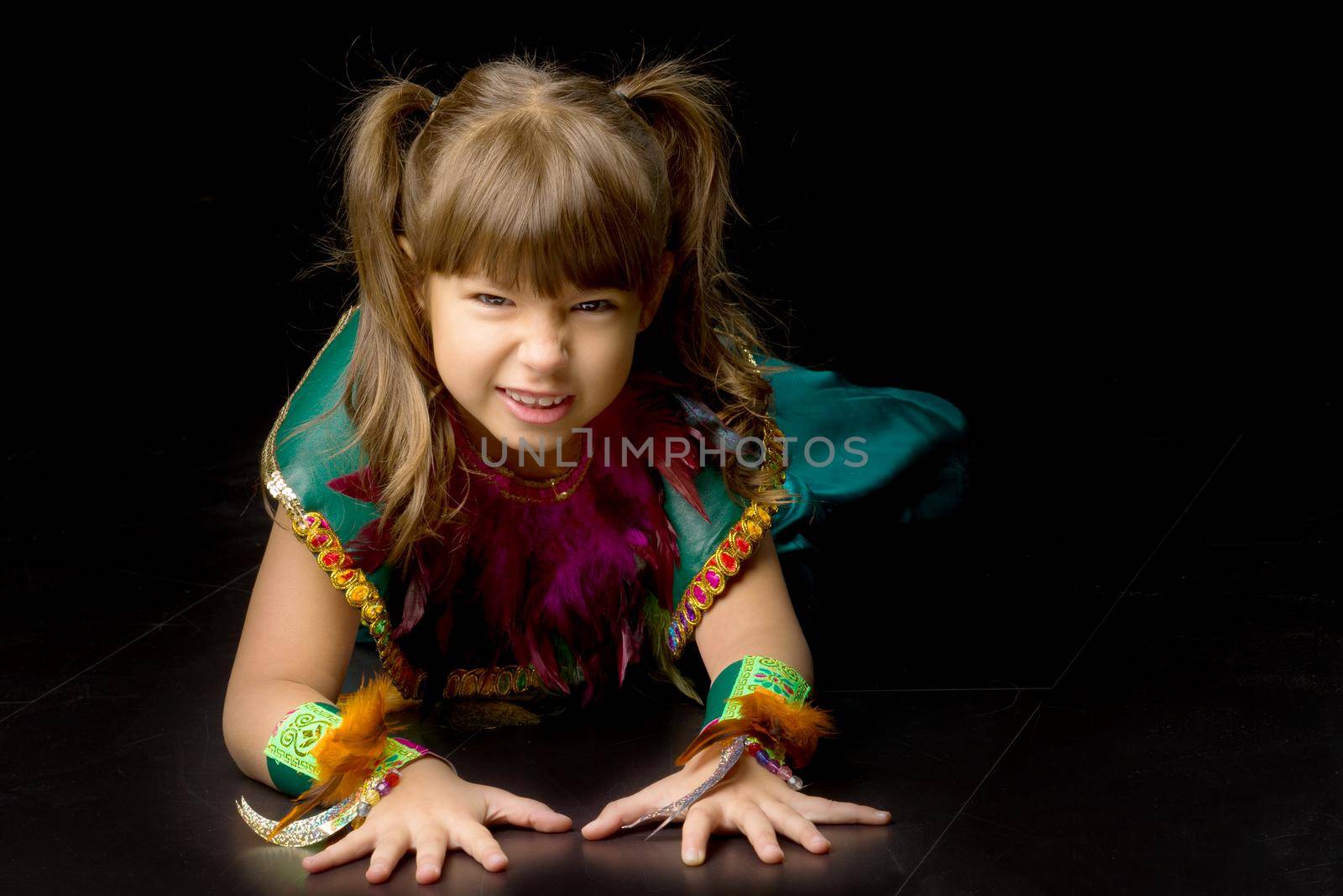 Pretty little girl crawling on floor. Portrait of beautiful preteen girl dressed bright ethnic costume posing on black background. Emotional child sitting on floor in studio