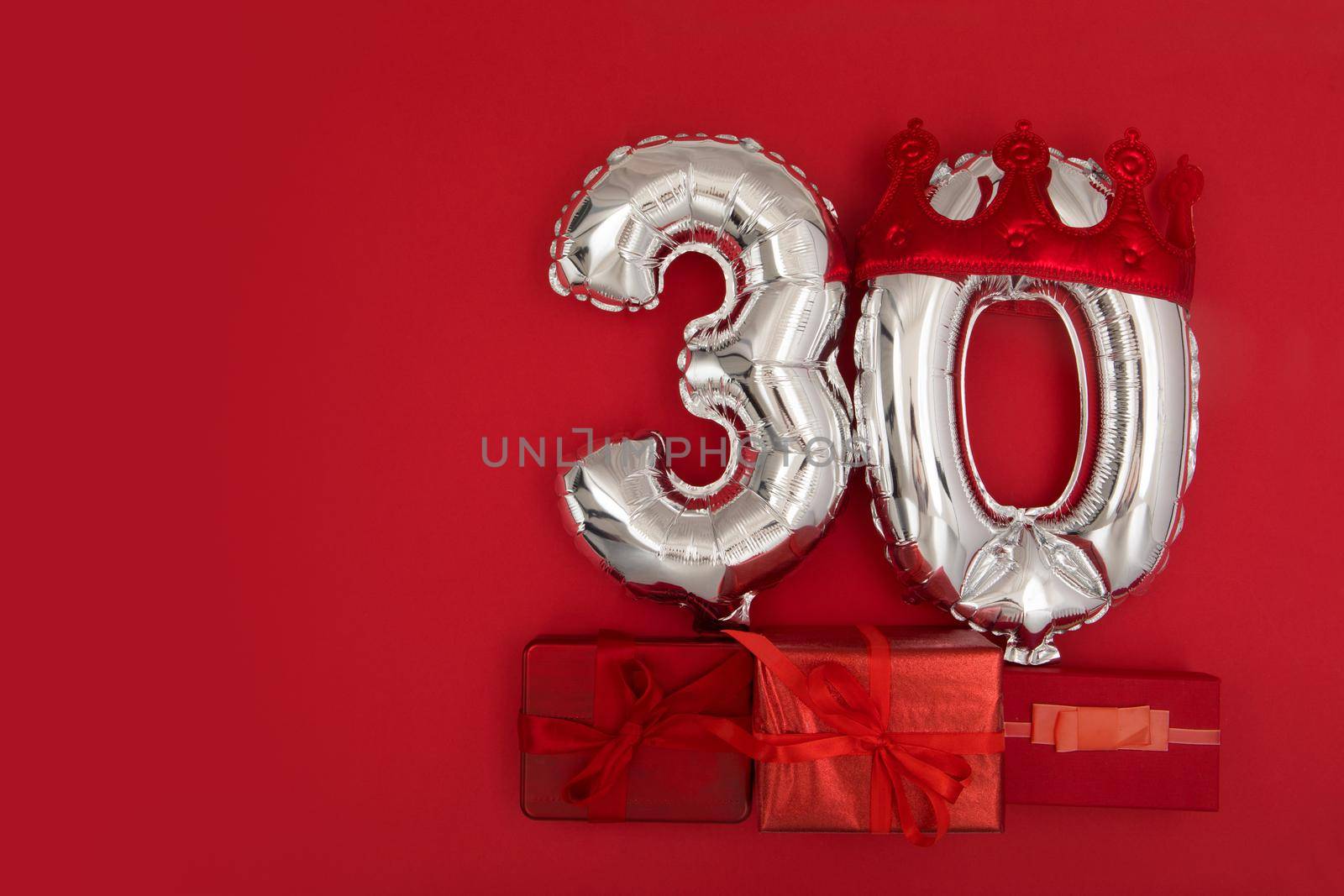 Foil silver air balloons showing number thirty placed on red background with wrapped presents for concept of birthday anniversary