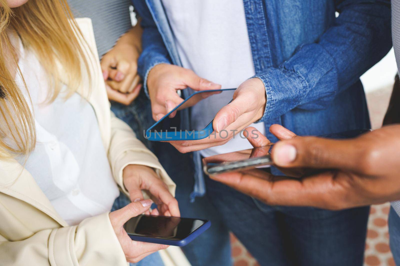 Hands of young unrecognizable people using smartphone outdoors.