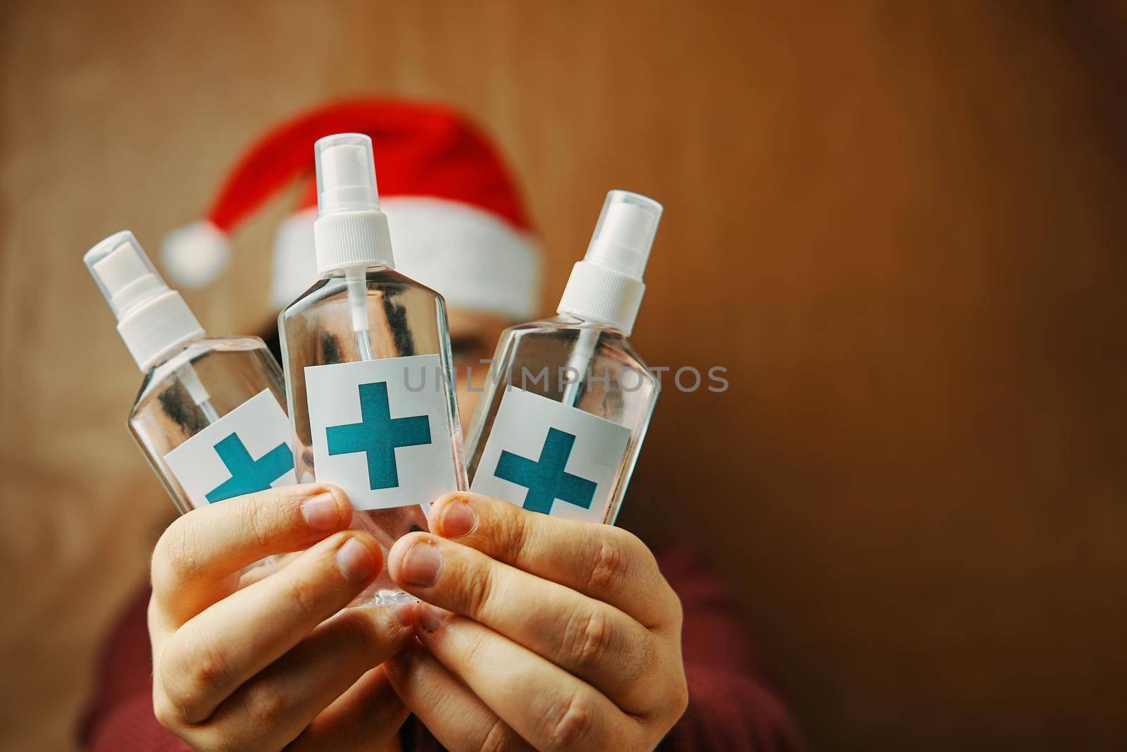 Sanitizers with turquoise cross on label in hands. Man in red Santa hat. Christmas in quarantine. New year's prevention against viruses and bacteria.