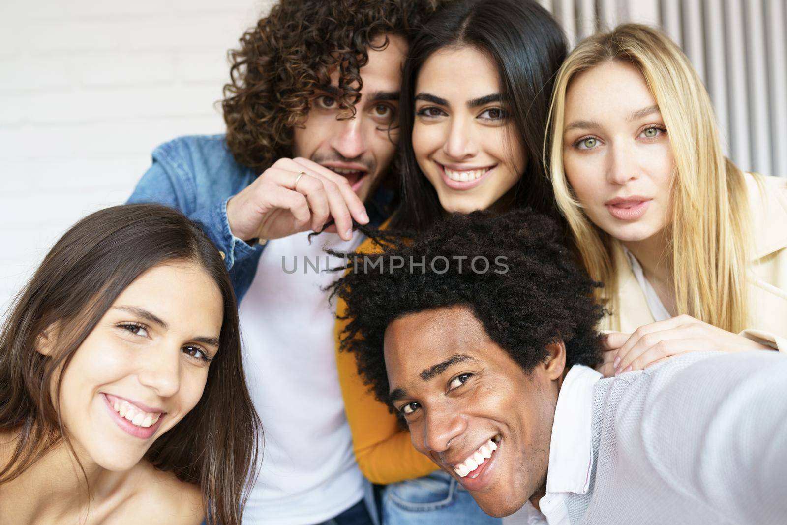 Multi-ethnic group of friends taking a selfie together while having fun in the street. Black man with afro hair in the foreground.