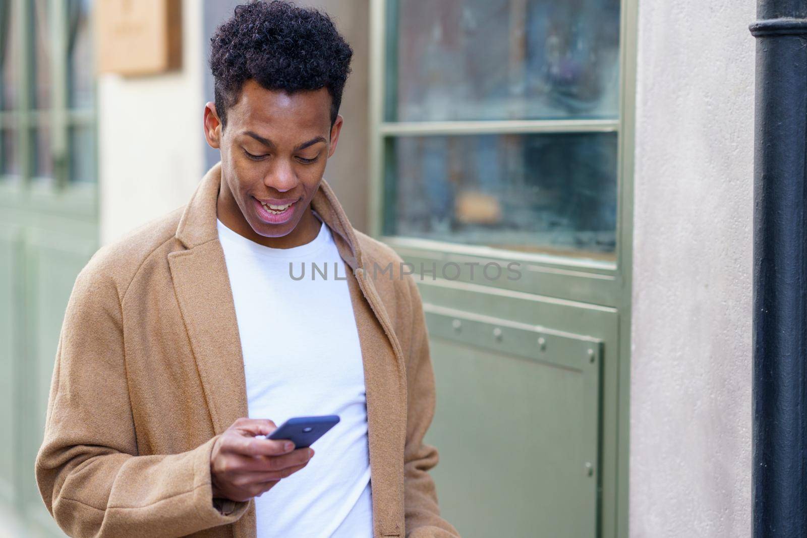 Young black man consulting his phone while walking down the street. Cuban guy in urban background.