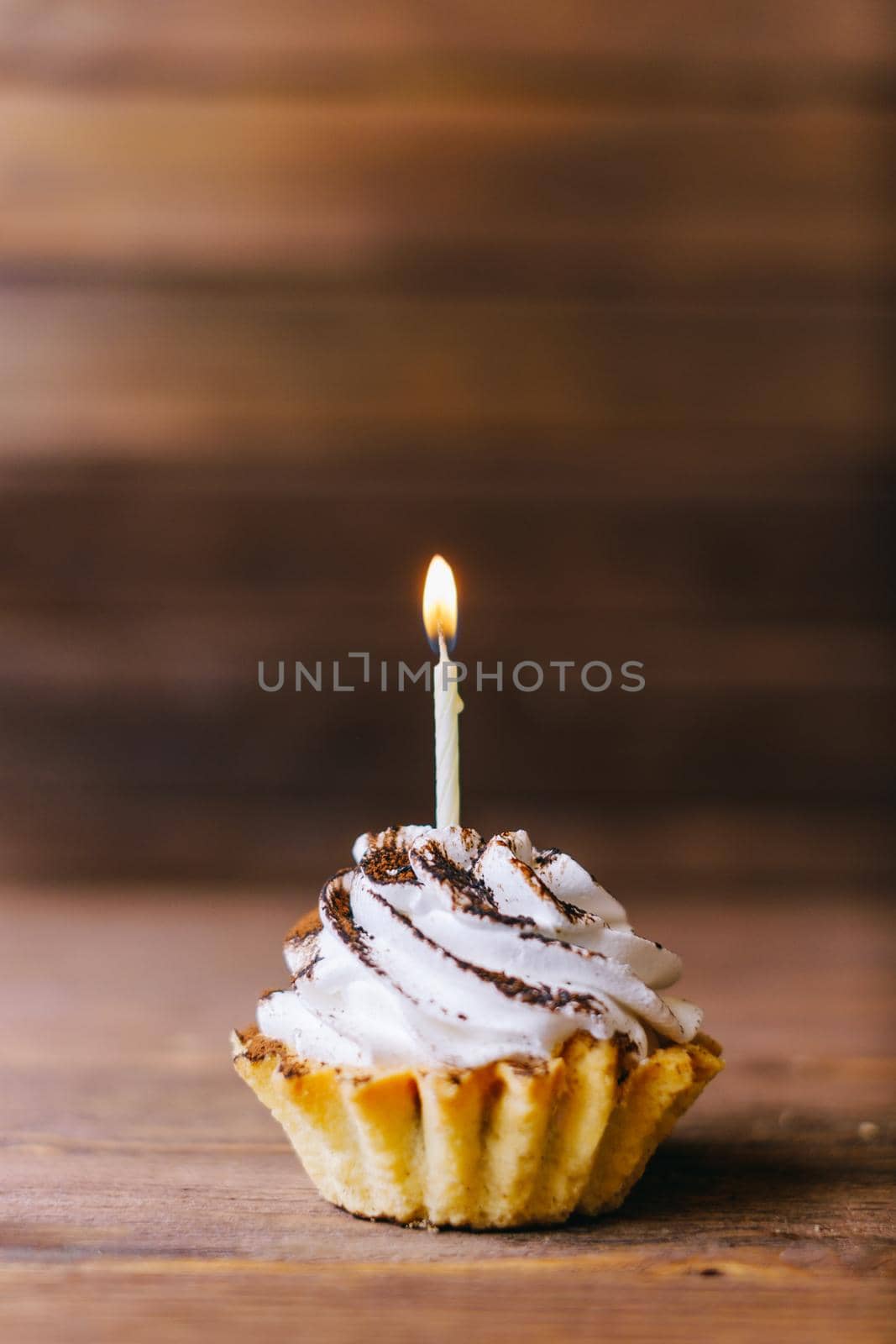 Birthday cream cupcake with one candle on a wooden background.